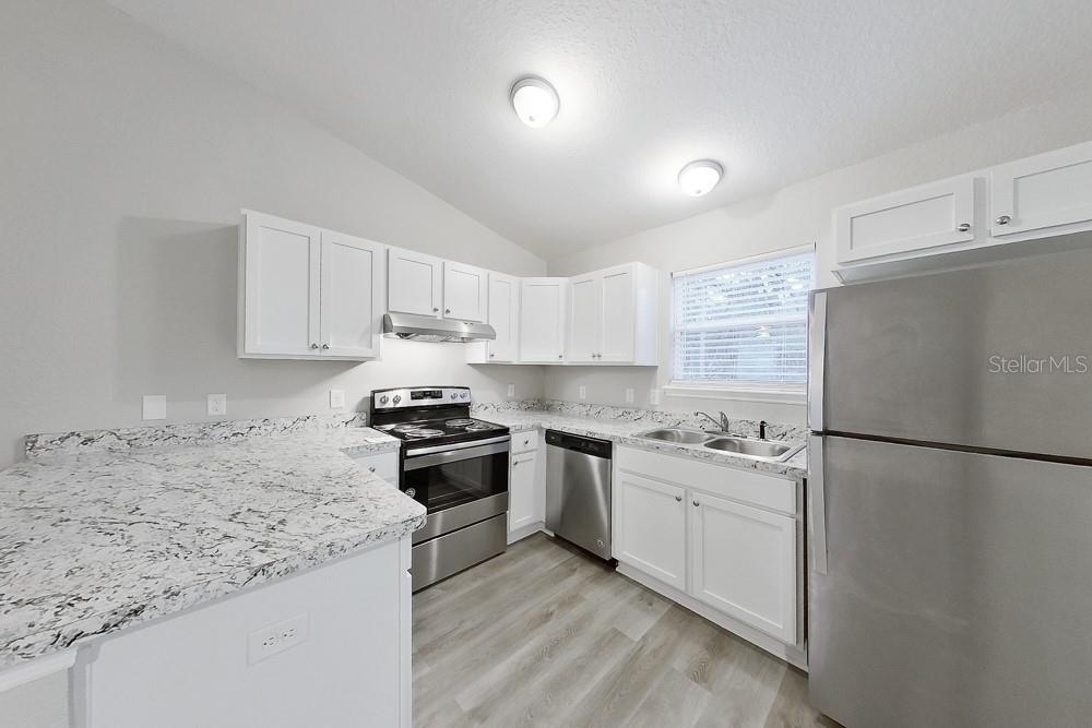 A kitchen features white cabinets, granite countertops, stainless steel appliances, and light wood-look flooring — 6771 SW 149TH LANE ROAD, OCALA, FL