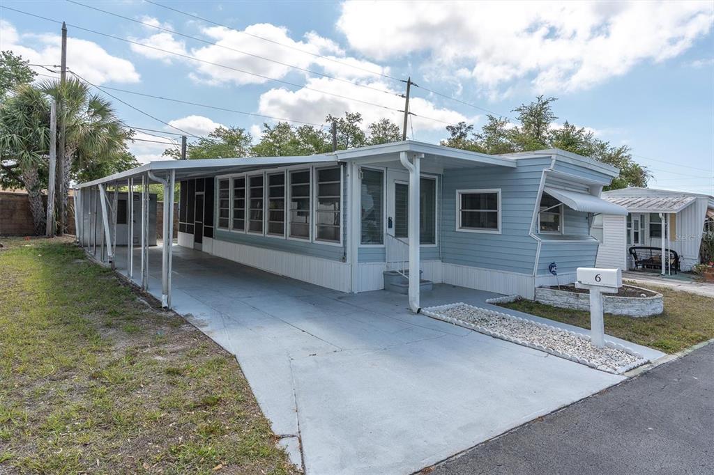 A light blue mobile home features a long carport, a screened-in porch, and a driveway — 7801 34TH AVENUE N UNIT 6, ST PETERSBURG, FL