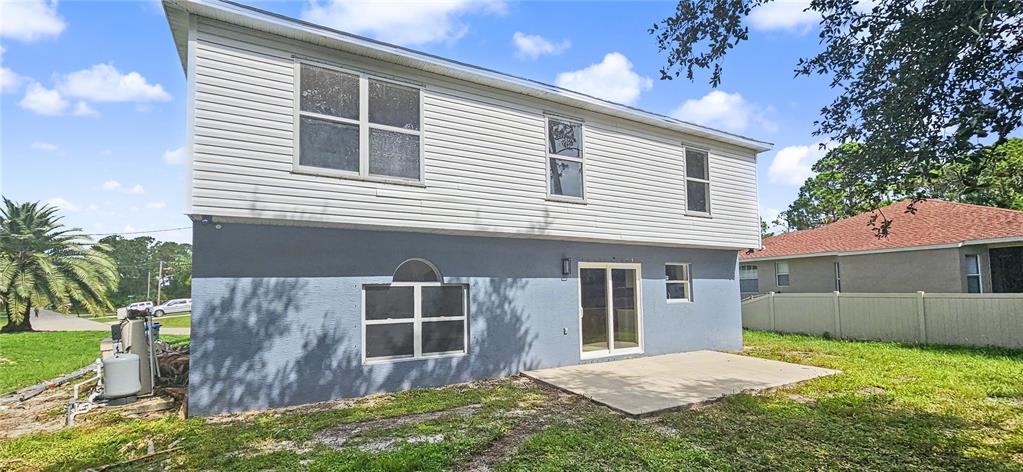 The rear exterior of a two-story house features white siding, a gray stucco base, and a patio — 4948 CROMEY ROAD, NORTH PORT, FL