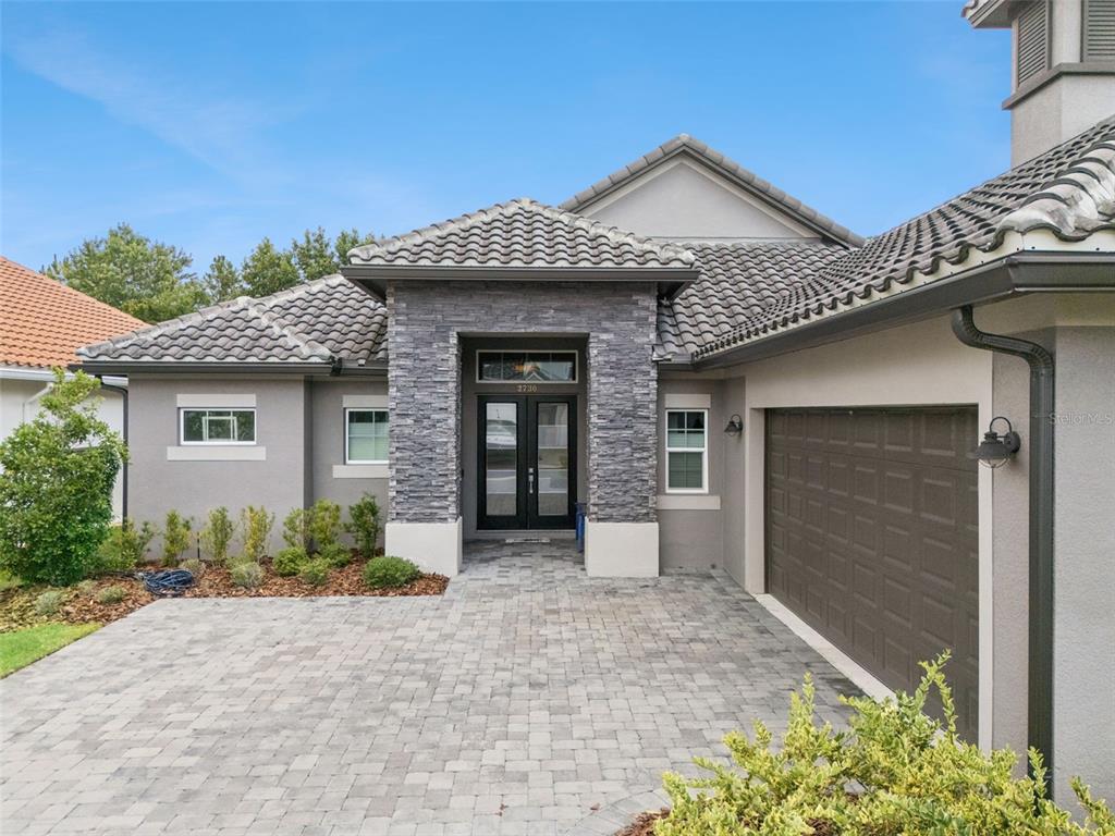 A gray stucco house features a stone-accented entryway, a tiled roof, and a paved driveway — 2730 WILLINGAM DRIVE, DAVENPORT, FL