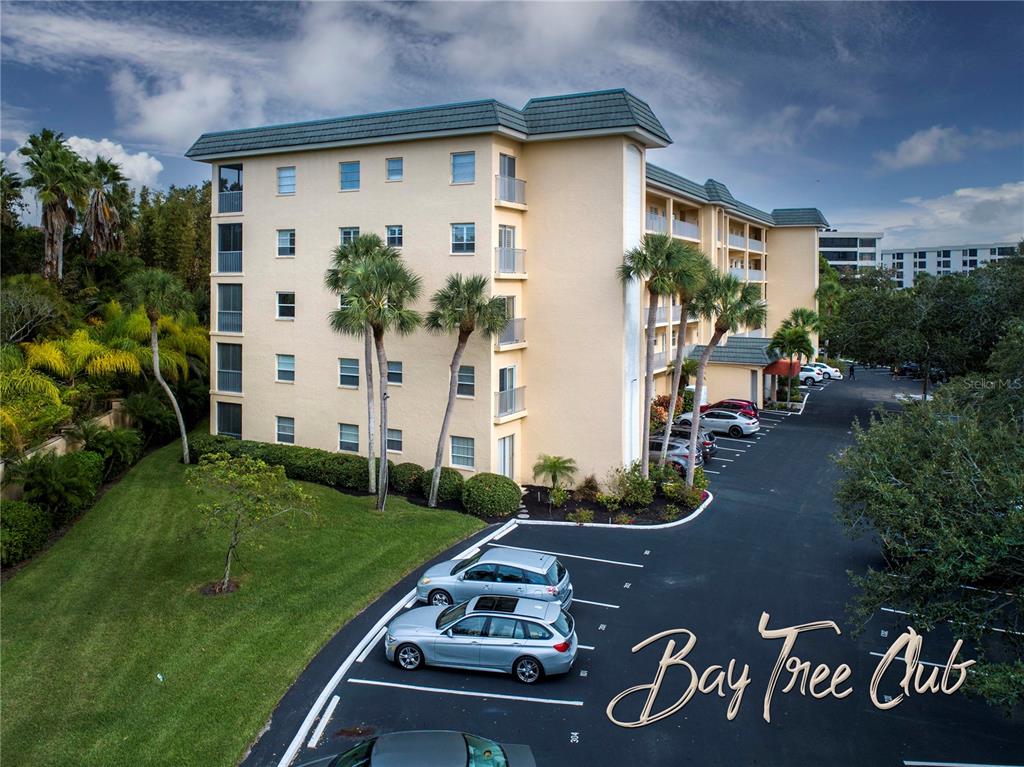 An exterior view of a multi-story apartment building with a parking lot in the foreground — 8625 MIDNIGHT PASS ROAD UNIT B508, SARASOTA, FL