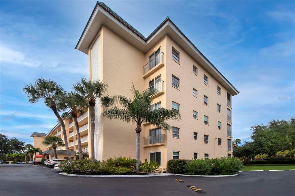 A multi-story beige apartment building with balconies and palm trees in the foreground — 8625 MIDNIGHT PASS ROAD UNIT B508, SARASOTA, FL