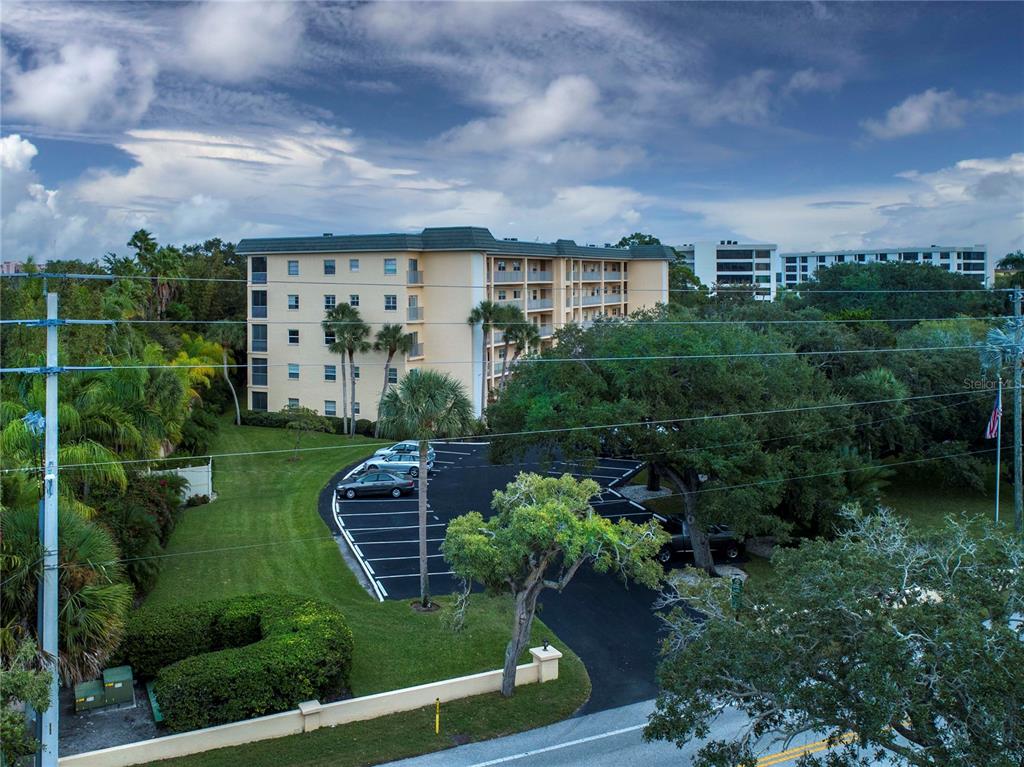 An exterior view of a multi-story apartment building with a parking lot and surrounding trees — 8625 MIDNIGHT PASS ROAD UNIT B508, SARASOTA, FL