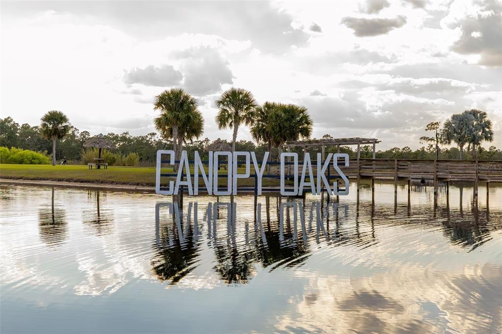 A sign reading Canopy Oaks stands in a pond near a wooden pier and palm trees — 104 HIGHWAY 630 E, LAKE WALES, FL