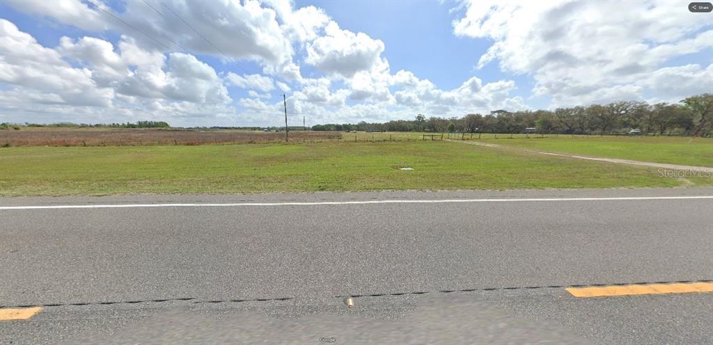 A flat, grassy vacant lot sits adjacent to a paved road under a cloudy sky — GREEN POND RD, POLK CITY, FL