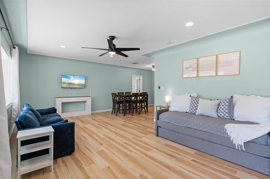 A living room with light blue walls, wood-look flooring, a daybed, and a dining area — 7690 91ST STREET, SEMINOLE, FL
