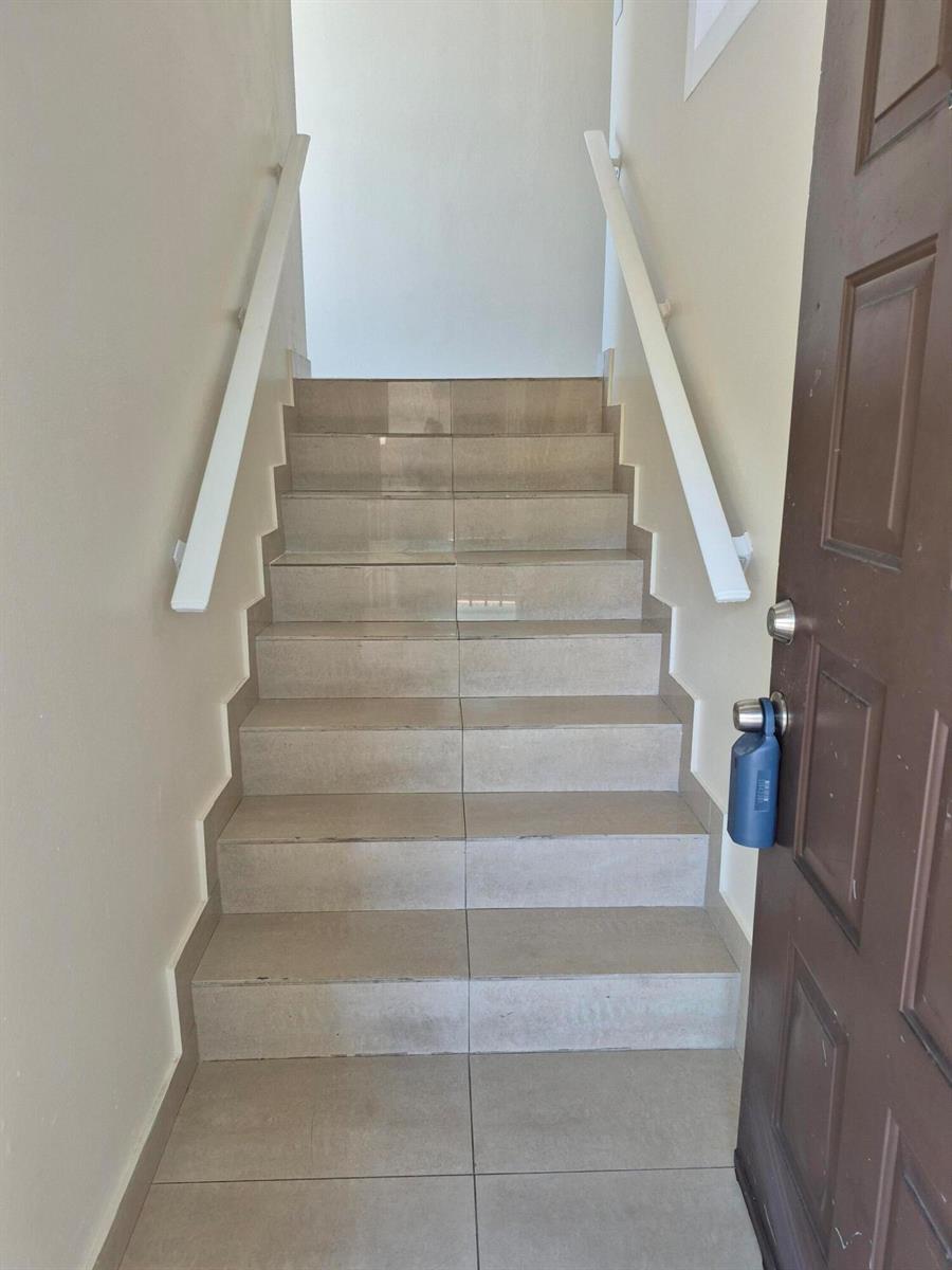 A staircase with beige tiled steps and white handrails leads upward from a doorway — 2823 N Course Drive # 205, Pompano Beach FL 33069, POMPANO BEACH, FL