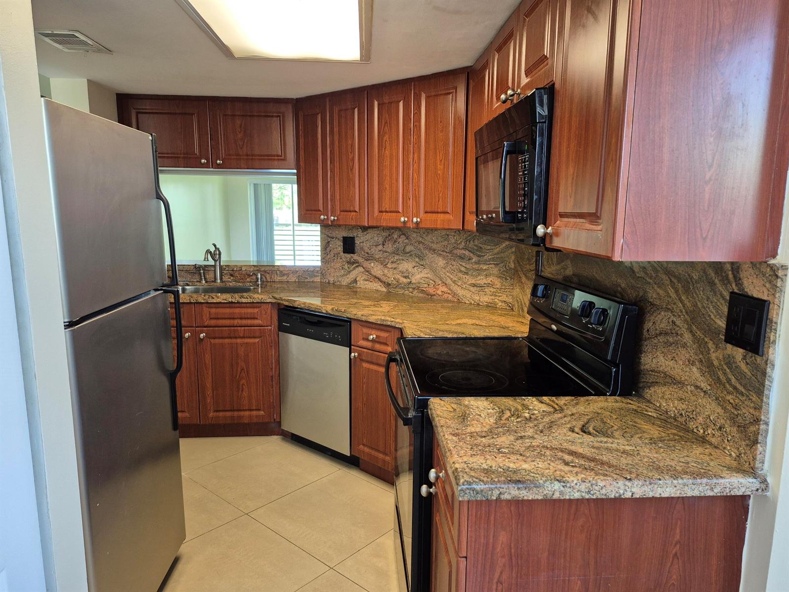 A kitchen features wood cabinets, granite countertops, stainless steel appliances, and light tile flooring — 2823 N Course Drive # 205, Pompano Beach FL 33069, POMPANO BEACH, FL