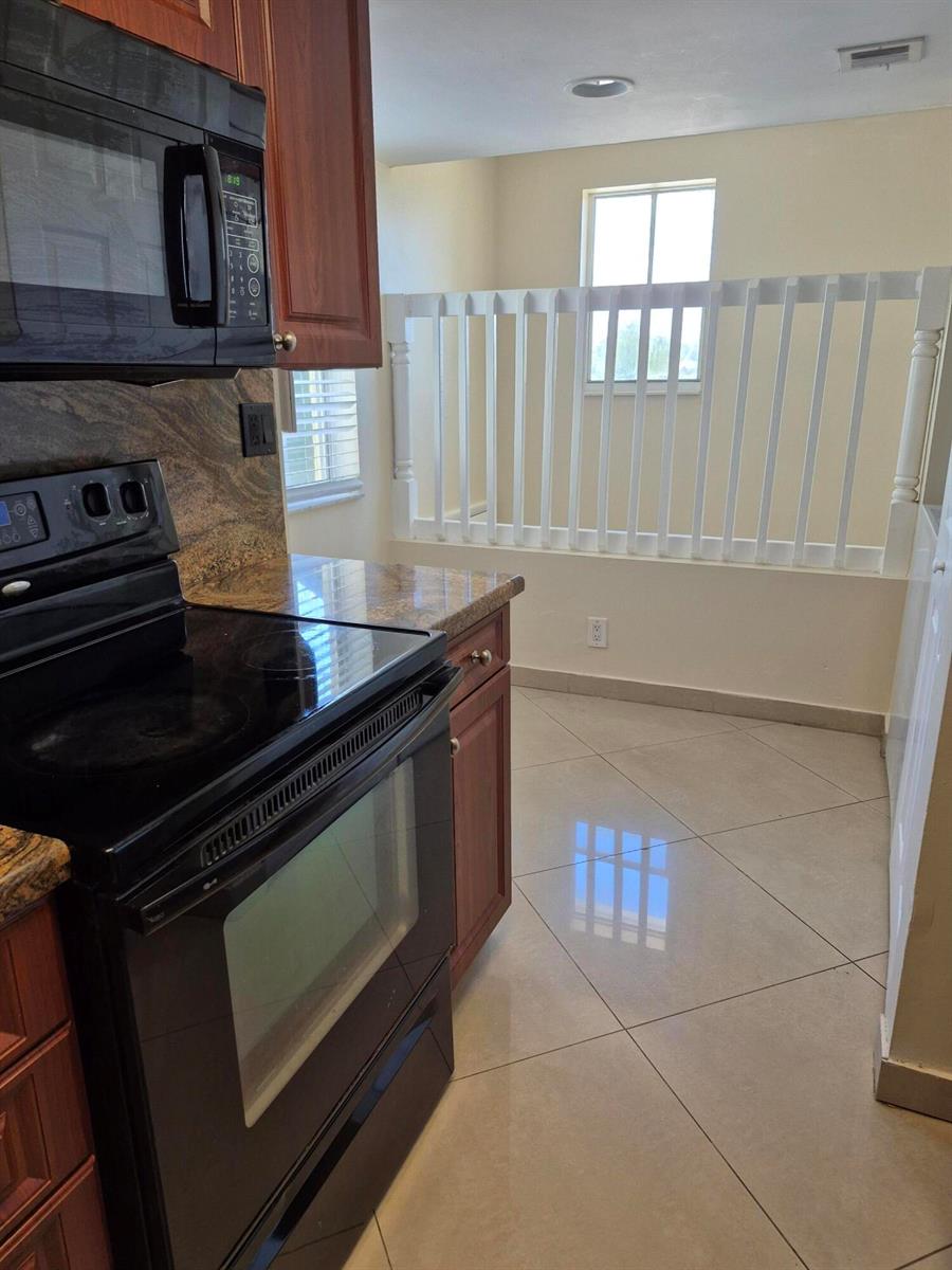A kitchen with dark wood cabinets, granite countertops, black appliances, and a white railing partition — 2823 N Course Drive # 205, Pompano Beach FL 33069, POMPANO BEACH, FL