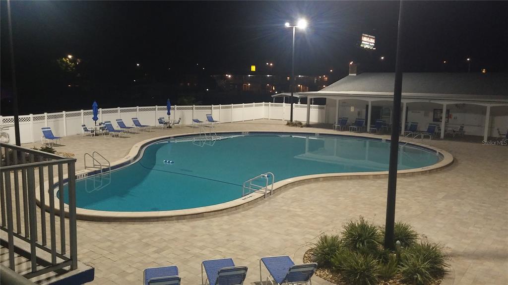 An outdoor swimming pool with lounge chairs and a covered patio at night — 57 HARBOR WAY UNIT 24, PALM HARBOR, FL