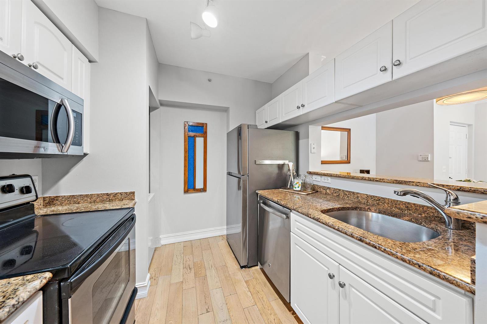 A kitchen features white cabinets, granite countertops, stainless steel appliances, and light wood flooring — 4117 Tuscany Way # 4117, Boynton Beach FL 33435, BOYNTON BEACH, FL
