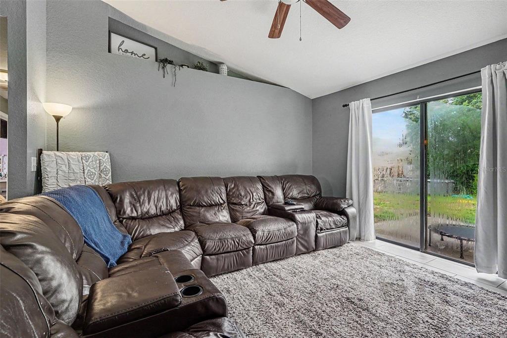 A living room features a large brown leather sectional, gray walls, and a sliding glass door — 2435 PARKLAND DRIVE, LAKELAND, FL