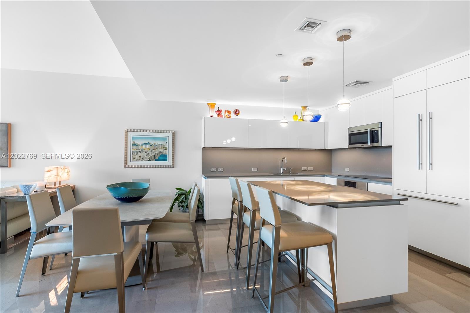 A modern kitchen and dining area feature white cabinetry, a stone island, and tile flooring — 68 SE 6th Street # 810, Miami FL 33131, MIAMI, FL