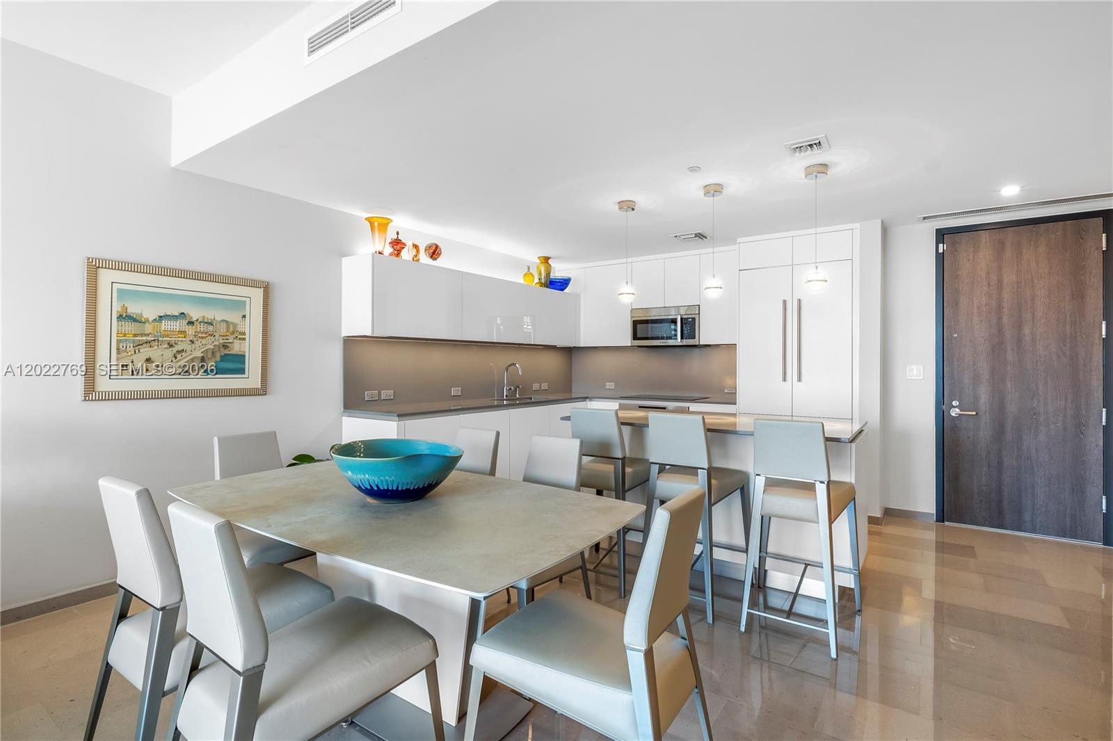 A modern kitchen features white cabinetry, a dining table with six chairs, and bar seating — 68 SE 6th Street # 810, Miami FL 33131, MIAMI, FL