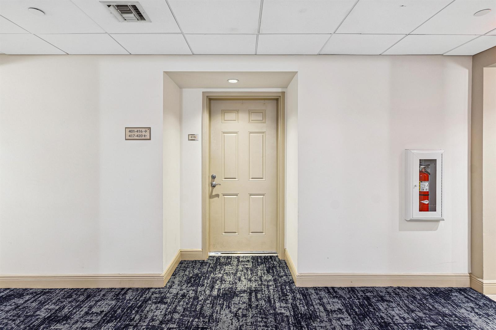 A beige door with a fire extinguisher cabinet is located in a carpeted hallway — 511 Lucerne Avenue # 416, FL 33460, FL