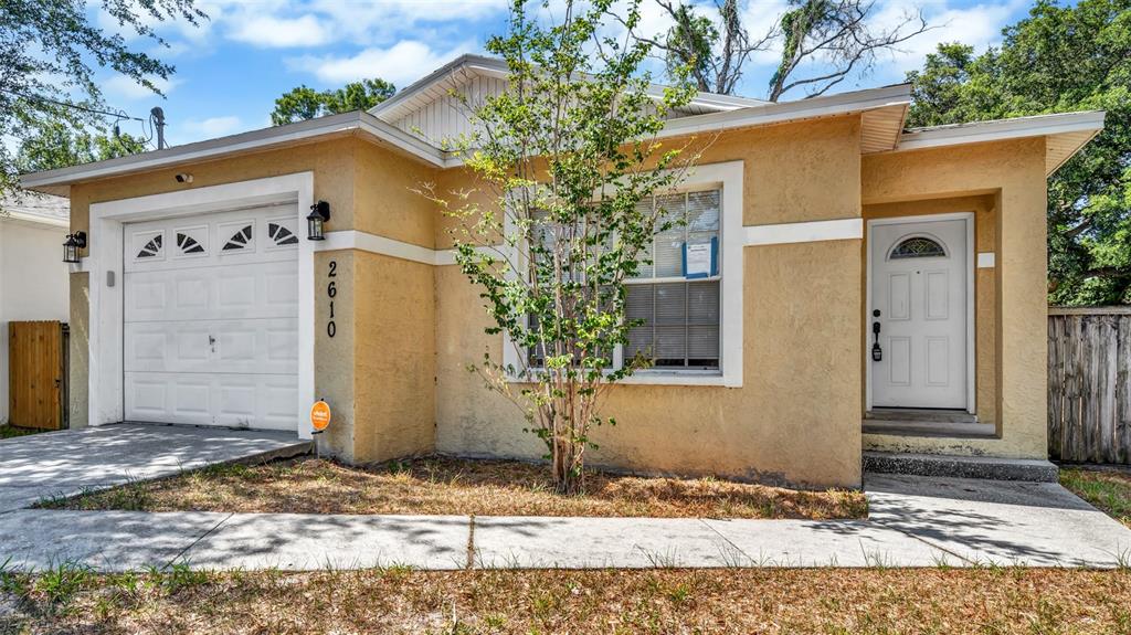 A single-story house with a tan stucco exterior, a one-car garage, and a front door — 2610 E LAKE AVENUE, TAMPA, FL