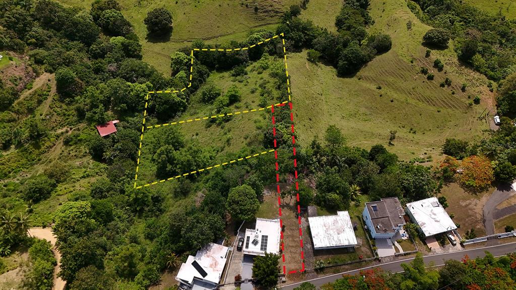 An aerial view shows a sloped, grassy lot outlined in yellow and red near houses — Km 1.1 CARR 400, RINCON, PR
