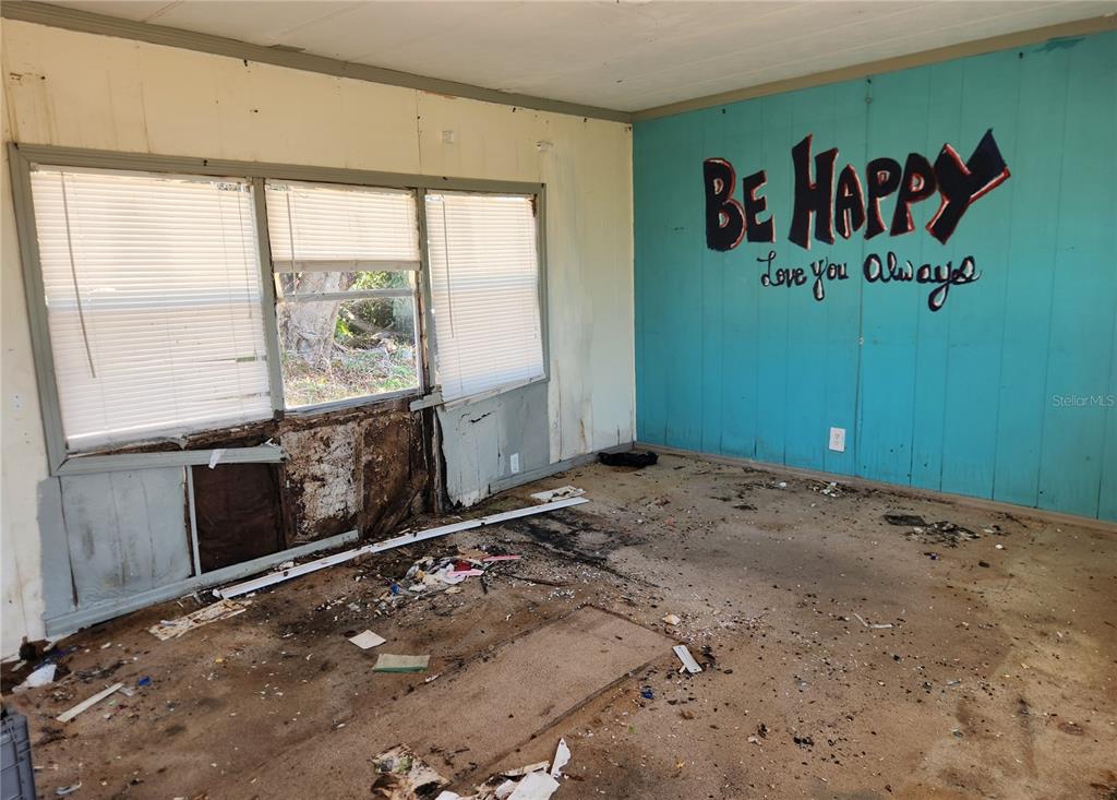 A dilapidated room features a teal wall with painted text and severe water-damaged wall panels — 3457 GAINSBORO ROAD, PORT CHARLOTTE, FL