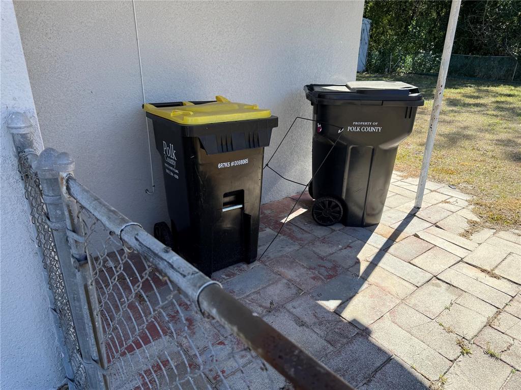 Two Polk County waste bins sit on a paved patio next to a chain-link fence — 204 6TH JPV STREET, WINTER HAVEN, FL
