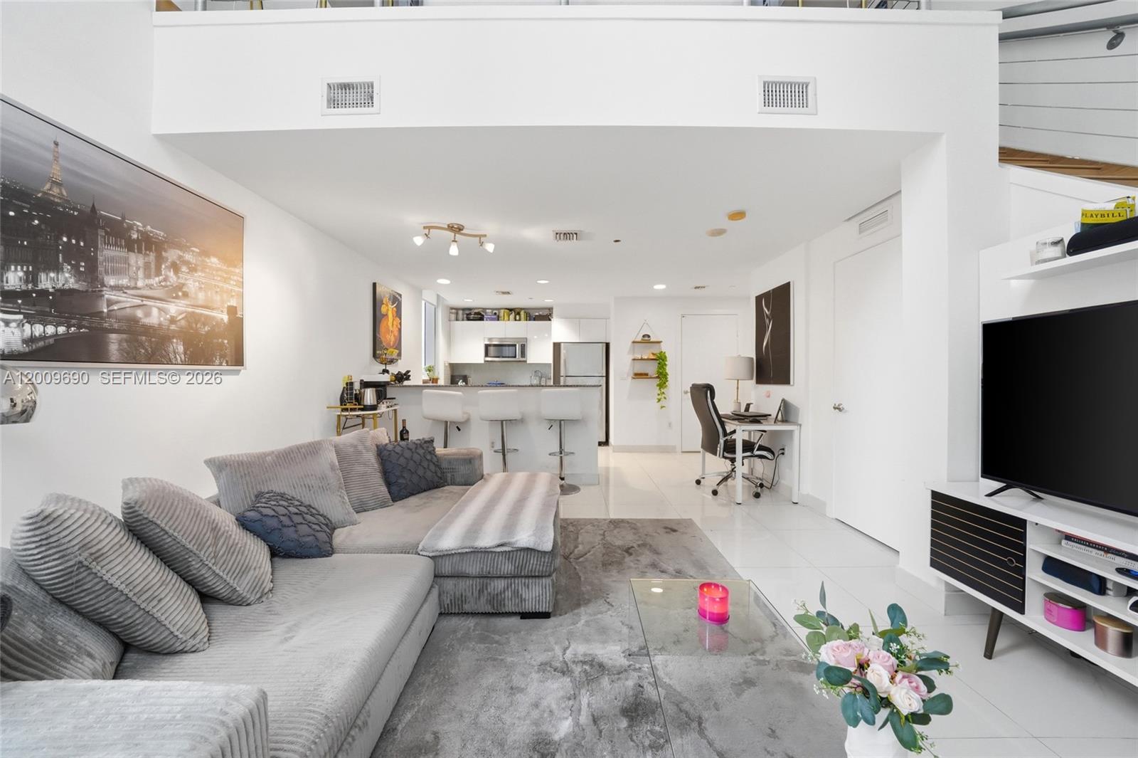 A modern living room features a grey sectional sofa, a television, and an open kitchen — 1050 Brickell Ave # 1002, Miami FL 33131, MIAMI, FL