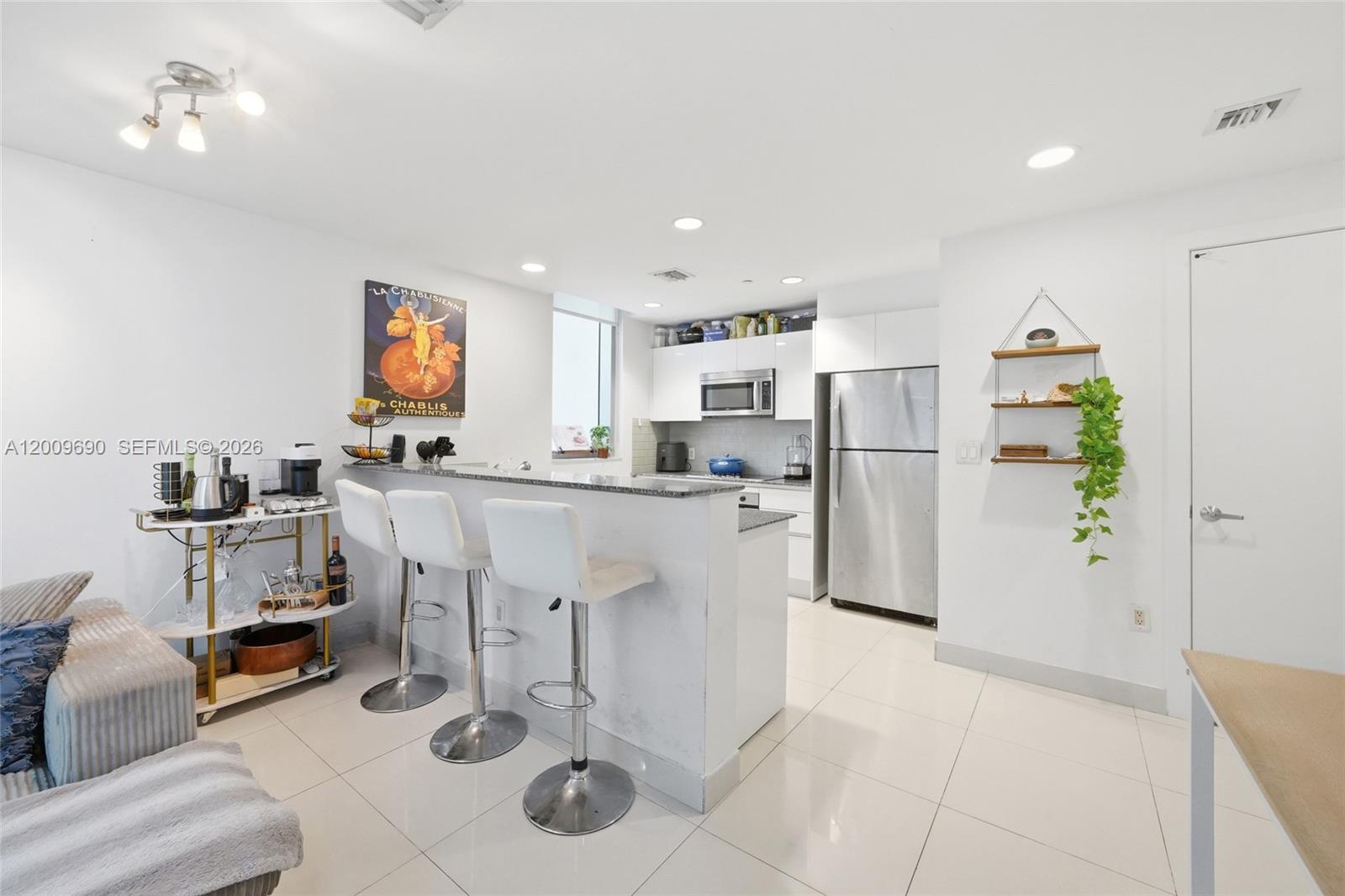 A modern kitchen features white cabinetry, stainless steel appliances, a breakfast bar, and tile flooring — 1050 Brickell Ave # 1002, Miami FL 33131, MIAMI, FL