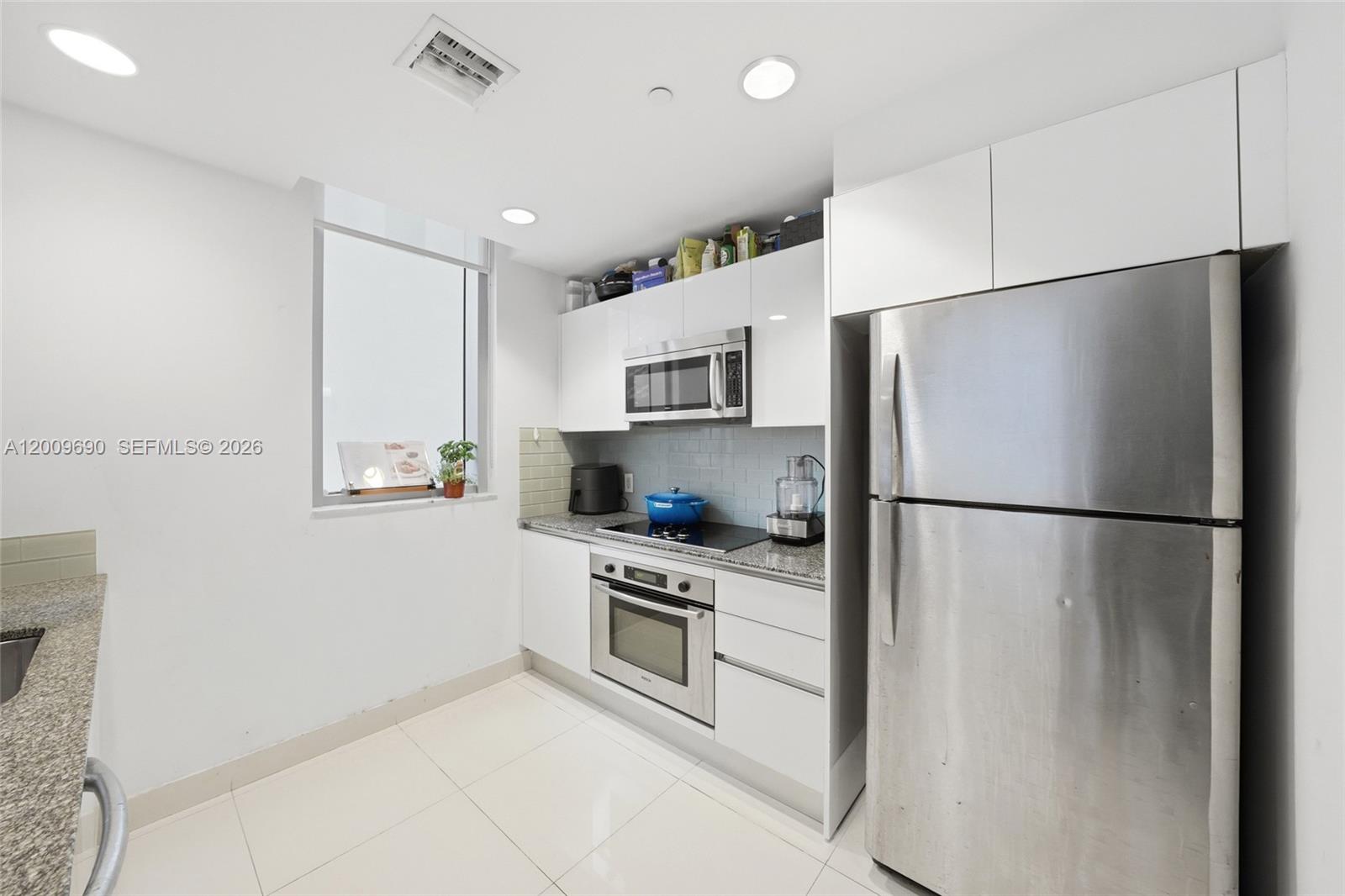 A modern kitchen features white cabinets, stainless steel appliances, and light-colored tile flooring — 1050 Brickell Ave # 1002, Miami FL 33131, MIAMI, FL