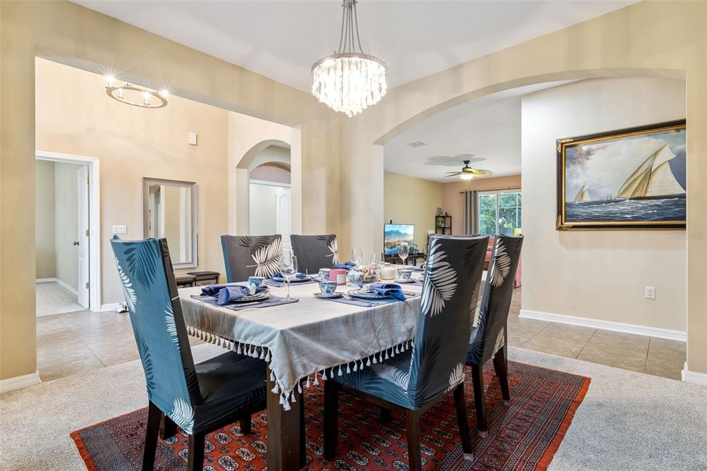 A dining room features a table with patterned chairs, a crystal chandelier, and an arched entryway — 2028 MISTY GLEN DRIVE, APOPKA, FL