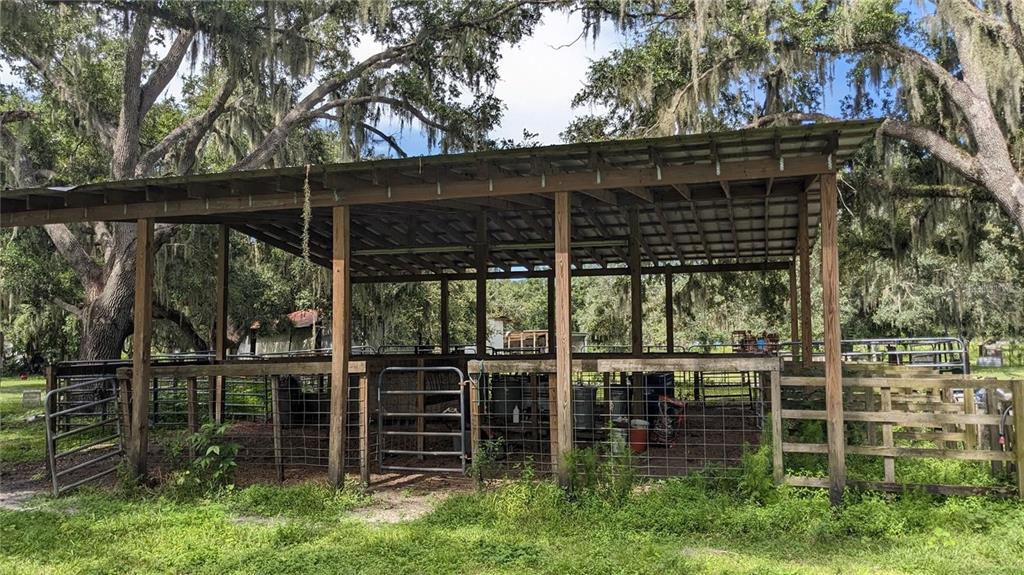 An open-sided wooden pole barn with metal roofing stands in a grassy, tree-filled area — 12980 and 12990 RIVER ROAD, MYAKKA CITY, FL