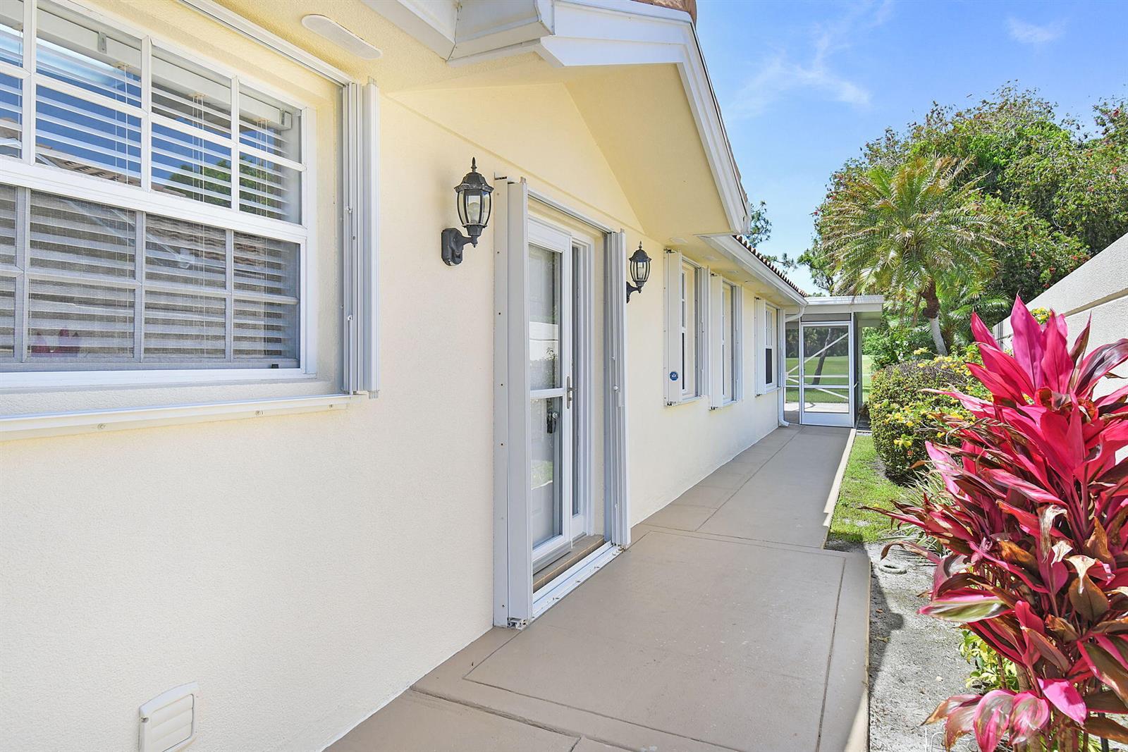 A beige exterior wall features a glass door, windows, and a concrete walkway — 7767 SE Spicewood Circle, Hobe Sound FL 33455, HOBE SOUND, FL