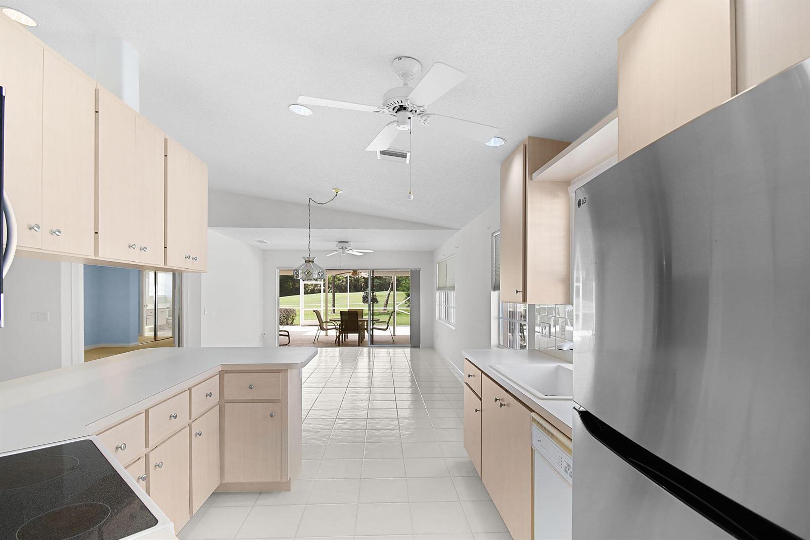 A kitchen with light wood cabinets, white countertops, and tile flooring opens to a dining area — 7767 SE Spicewood Circle, Hobe Sound FL 33455, HOBE SOUND, FL