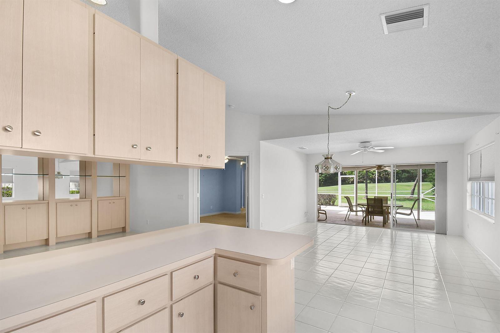 A kitchen with light wood cabinets overlooks a dining area with tile floors and sliding doors — 7767 SE Spicewood Circle, Hobe Sound FL 33455, HOBE SOUND, FL