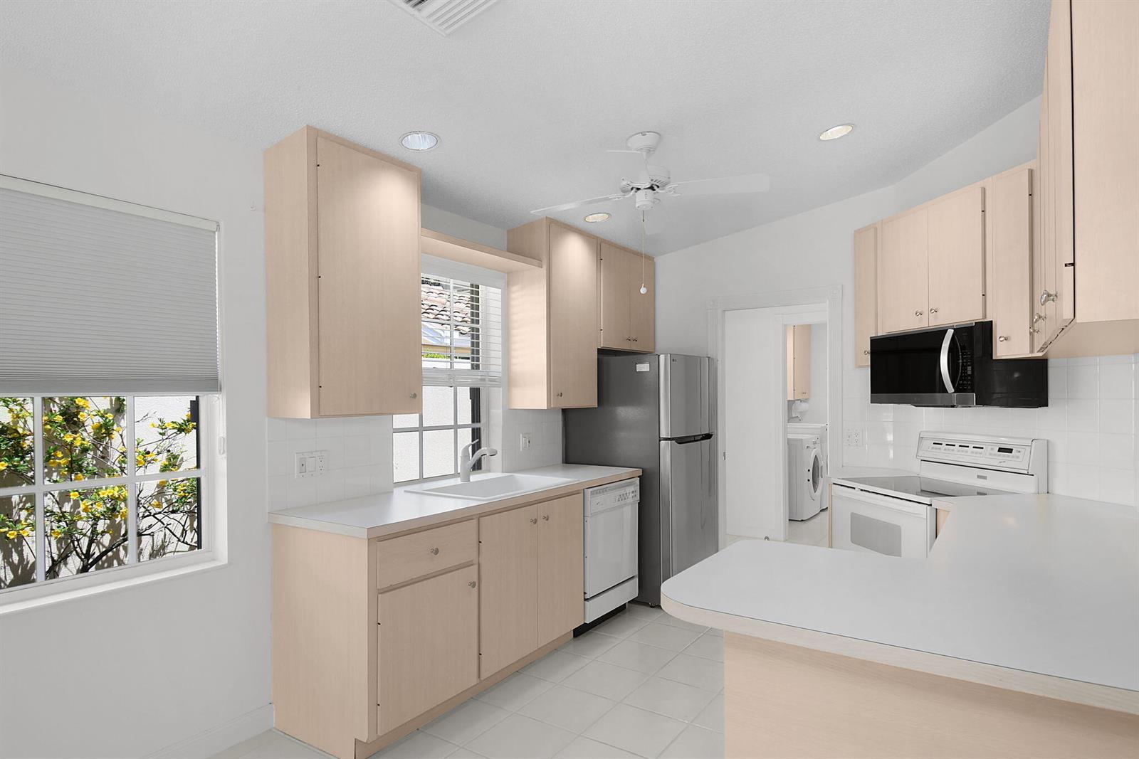 A kitchen features light wood cabinets, white countertops, a stainless steel refrigerator, and white appliances — 7767 SE Spicewood Circle, Hobe Sound FL 33455, HOBE SOUND, FL