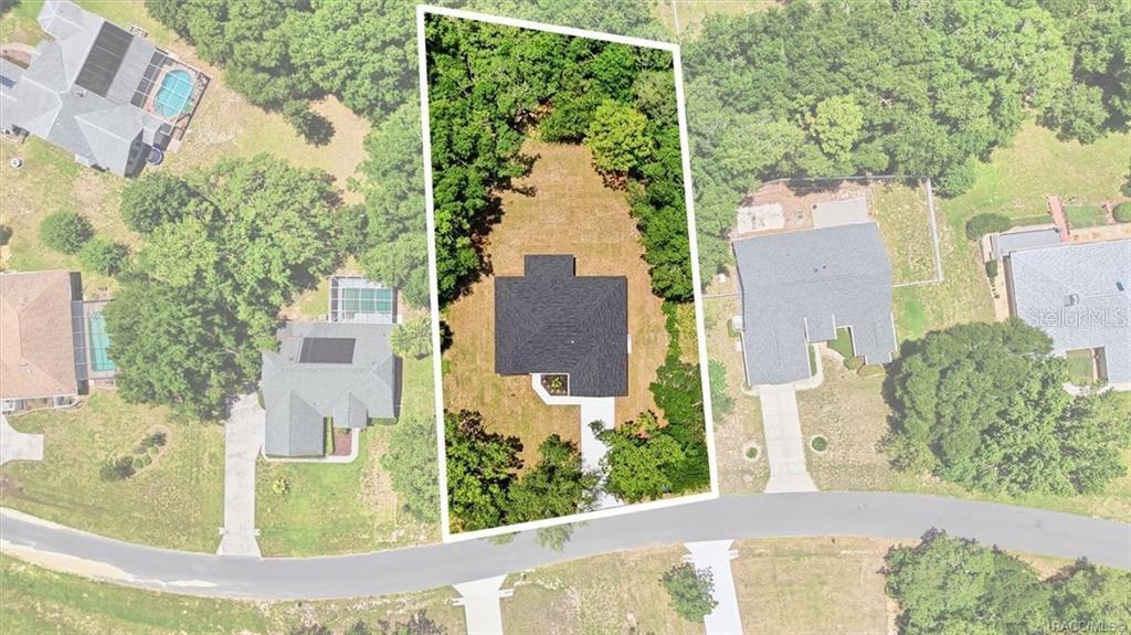 An aerial view shows a house with a black roof centered on a wooded lot — 1302 N MEDITERRANEAN WAY, INVERNESS, FL