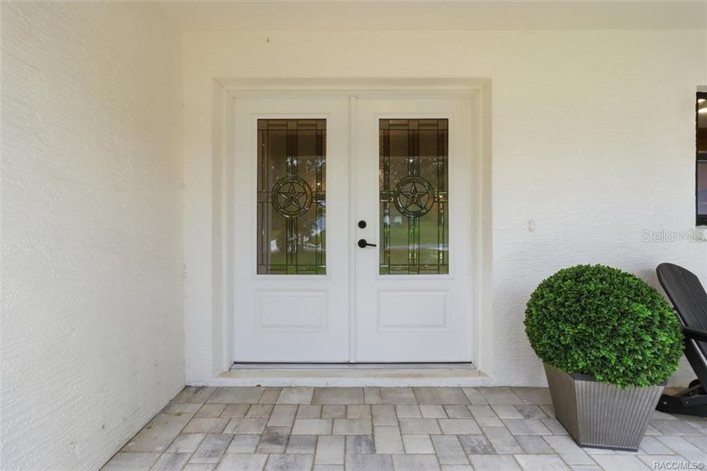 A white double front door with decorative glass panels sits on a paved porch — 1302 N MEDITERRANEAN WAY, INVERNESS, FL