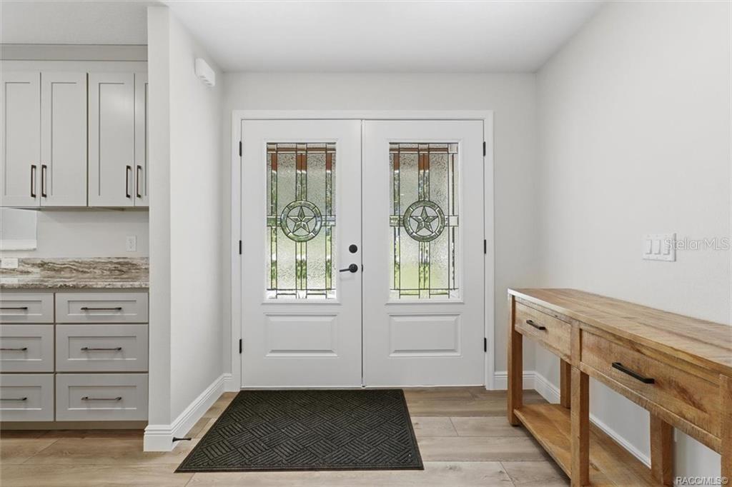 An entryway features double glass-paneled doors with star motifs, gray cabinets, and a wooden console — 1302 N MEDITERRANEAN WAY, INVERNESS, FL
