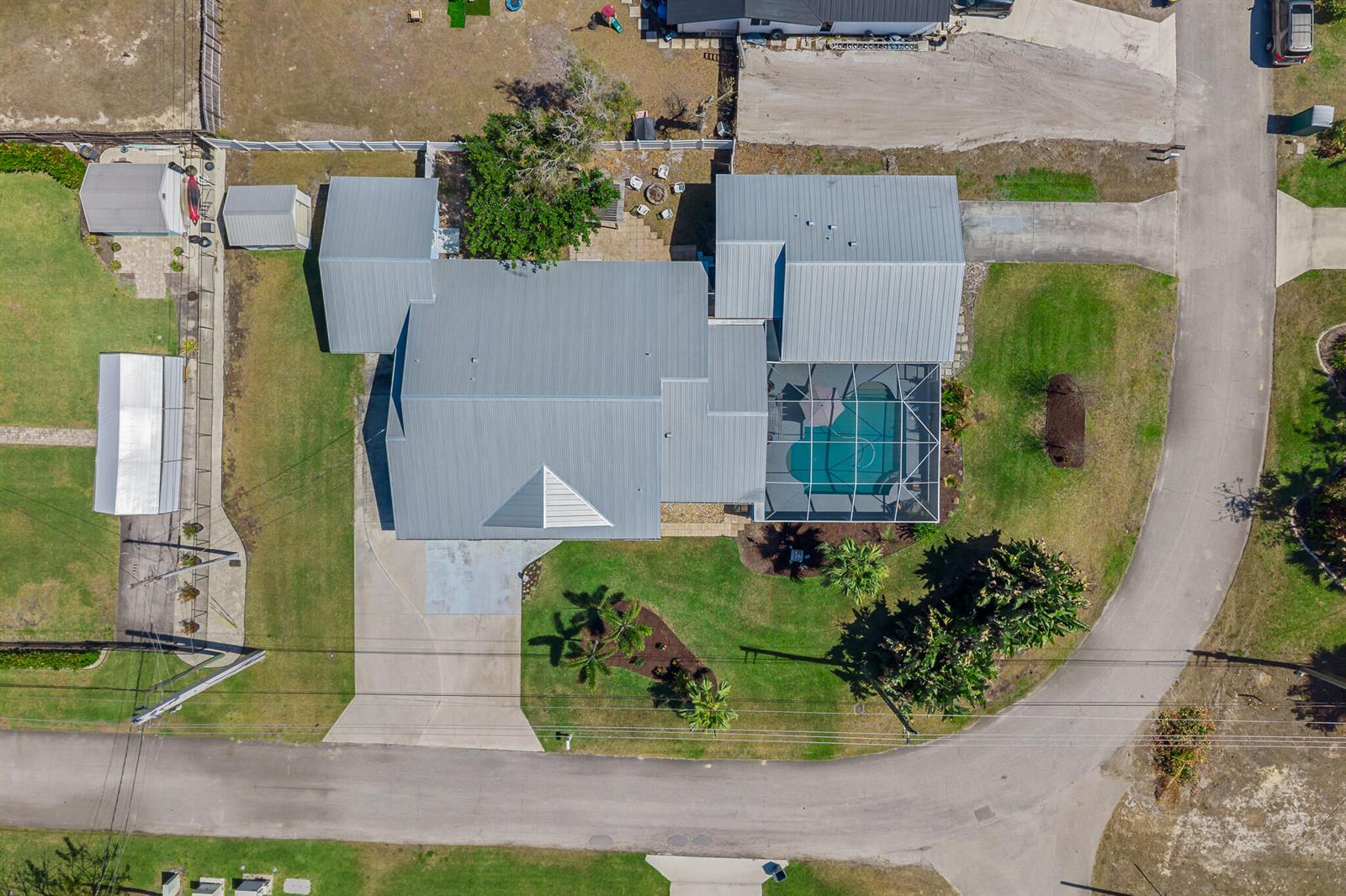 An aerial view shows a house with a metal roof, pool enclosure, and detached sheds — 4459 SE Kubin Avenue, Stuart FL 34997, STUART, FL