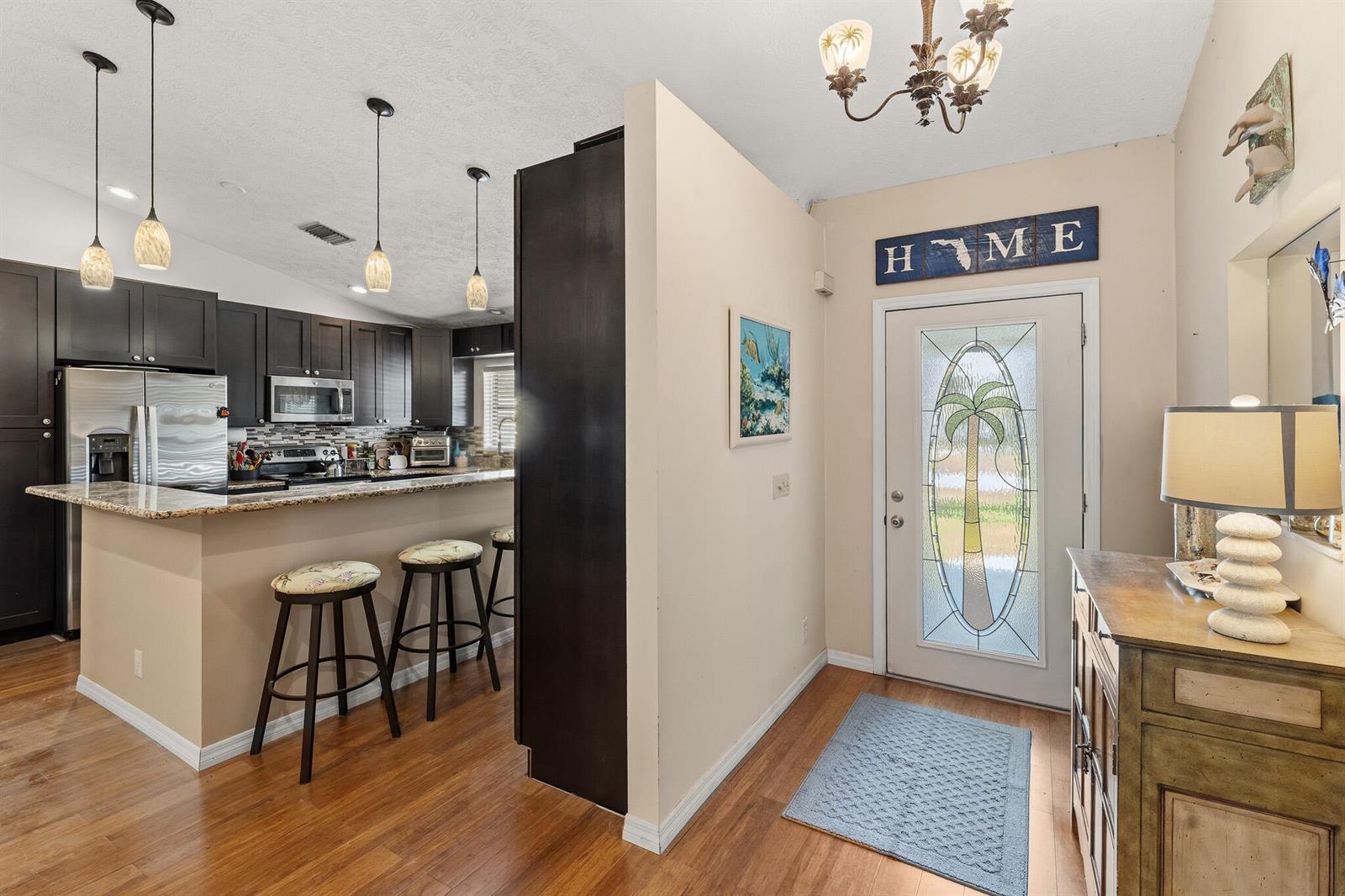 A kitchen with dark cabinets and a breakfast bar sits beside an entryway with a door — 4459 SE Kubin Avenue, Stuart FL 34997, STUART, FL