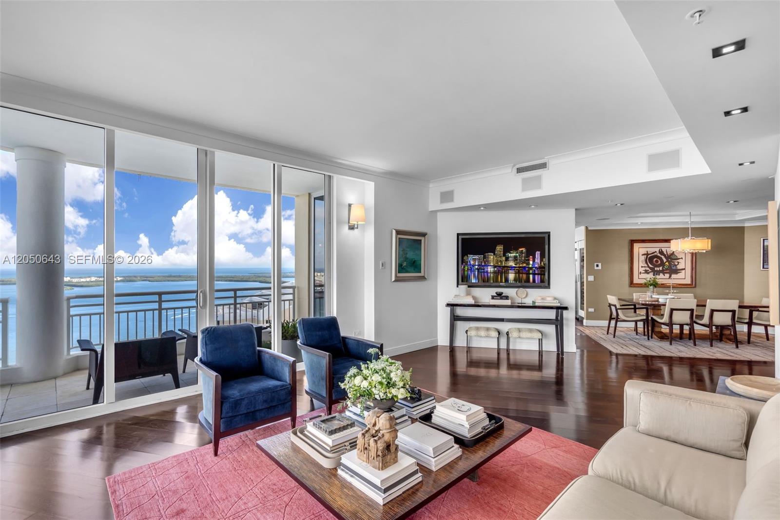 A living room with dark wood floors, blue armchairs, a pink rug, and a balcony view — 848 Brickell Key Drive, Miami FL 33131, MIAMI, FL