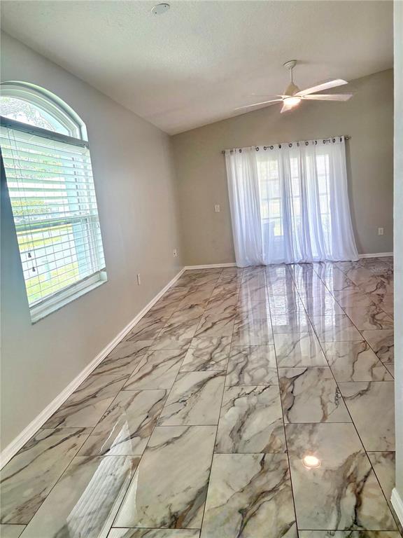 An empty room features large-format marble-look tile flooring, a vaulted ceiling, and sliding glass doors — 9221 ESTRADA PLACE, NEW PORT RICHEY, FL