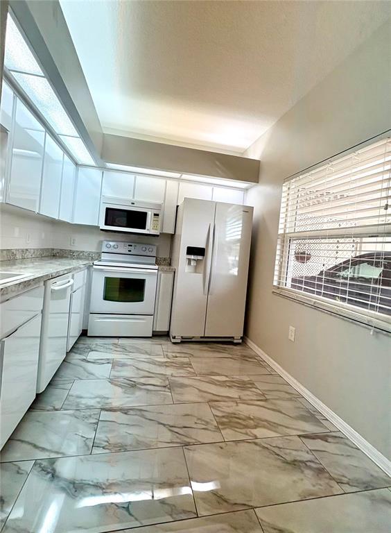 A kitchen with white cabinets, white appliances, and marble-patterned tile flooring — 9221 ESTRADA PLACE, NEW PORT RICHEY, FL