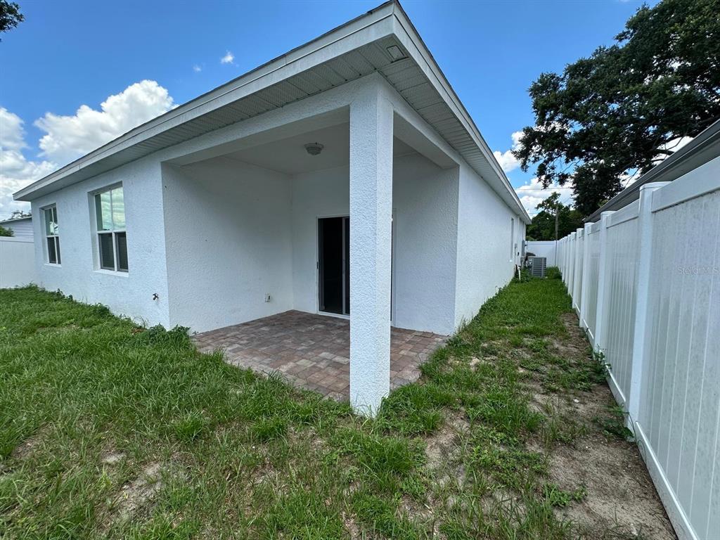 A covered patio with paver flooring sits at the rear of a white stucco house — 117 W MURPHY STREET, DAVENPORT, FL