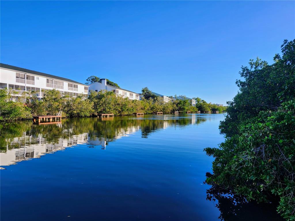 A calm canal reflects white multi-story residential buildings and surrounding green mangroves under a clear sky — 14883 SEMINOLE TRAIL UNIT 130, SEMINOLE, FL