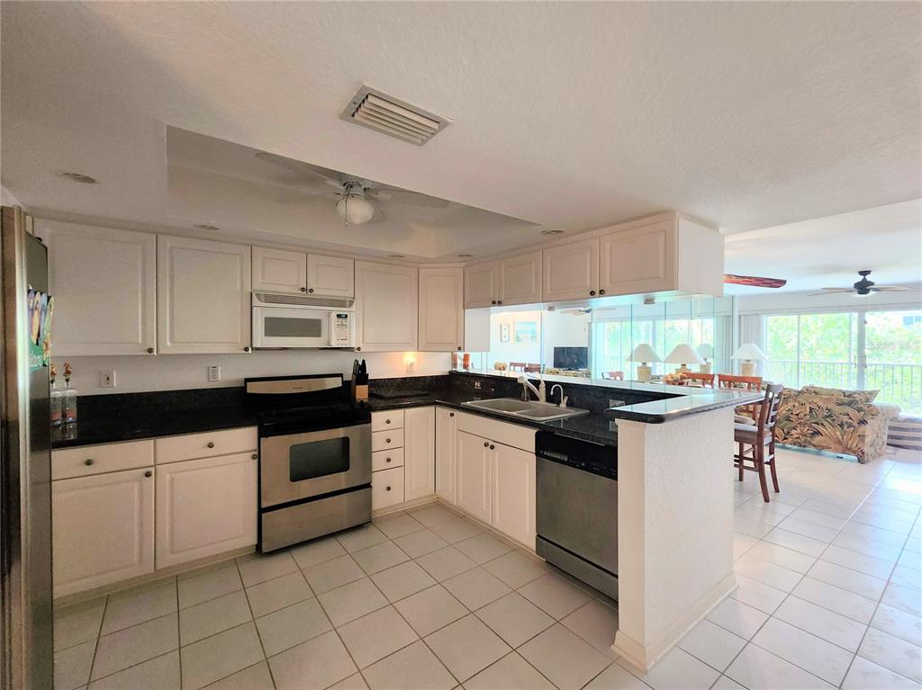 A kitchen with white cabinets, black countertops, and stainless steel appliances opens to a living area — 14883 SEMINOLE TRAIL UNIT 130, SEMINOLE, FL
