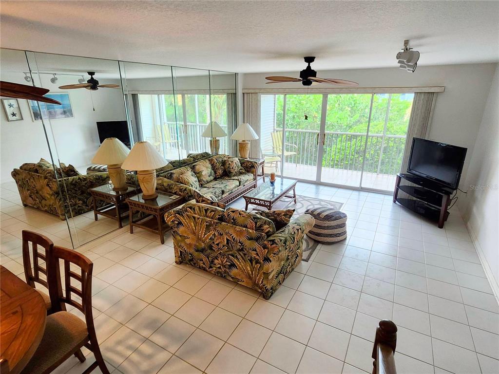 A living room features tiled floors, tropical-patterned furniture, mirrored walls, and a sliding glass door — 14883 SEMINOLE TRAIL UNIT 130, SEMINOLE, FL