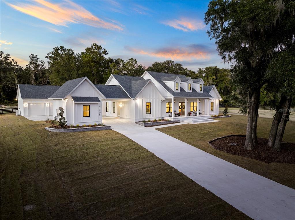 A white farmhouse with a gray roof and a concrete driveway sits on a grassy lot — 17104 SW 11TH COURT, NEWBERRY, FL