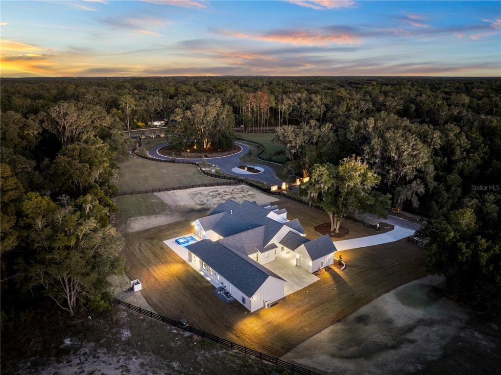An aerial view shows a white modern farmhouse with a pool surrounded by wooded land — 17104 SW 11TH COURT, NEWBERRY, FL