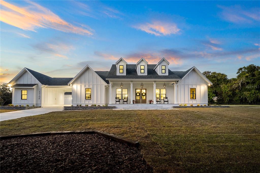 A white farmhouse with a covered porch and three dormers sits on a grassy lot — 17104 SW 11TH COURT, NEWBERRY, FL