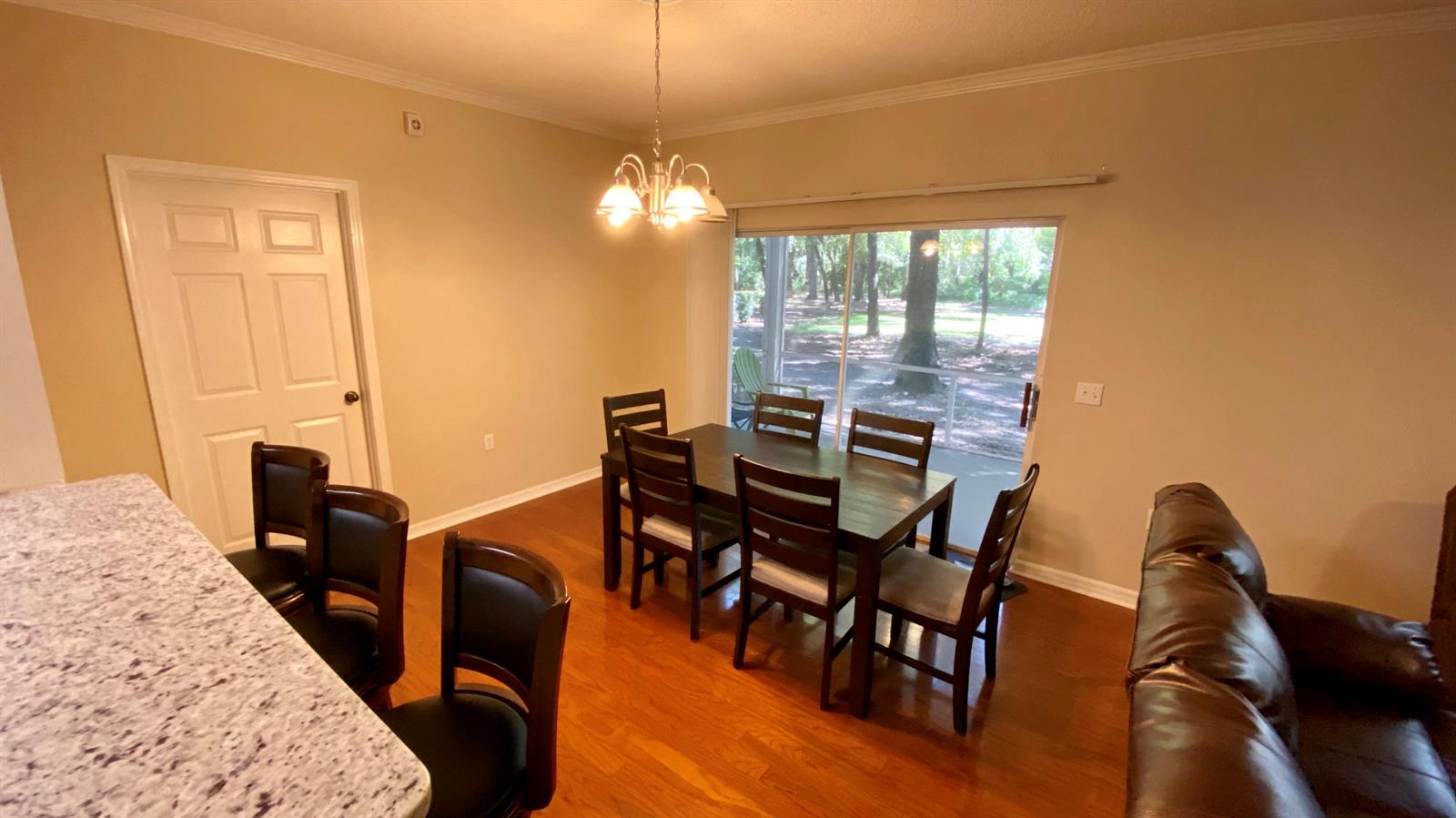 A dining area features a wooden table with six chairs, a chandelier, and sliding glass doors — 10000 SW 52nd Avenue # 76, Gainesville FL 32608, GAINESVILLE, FL