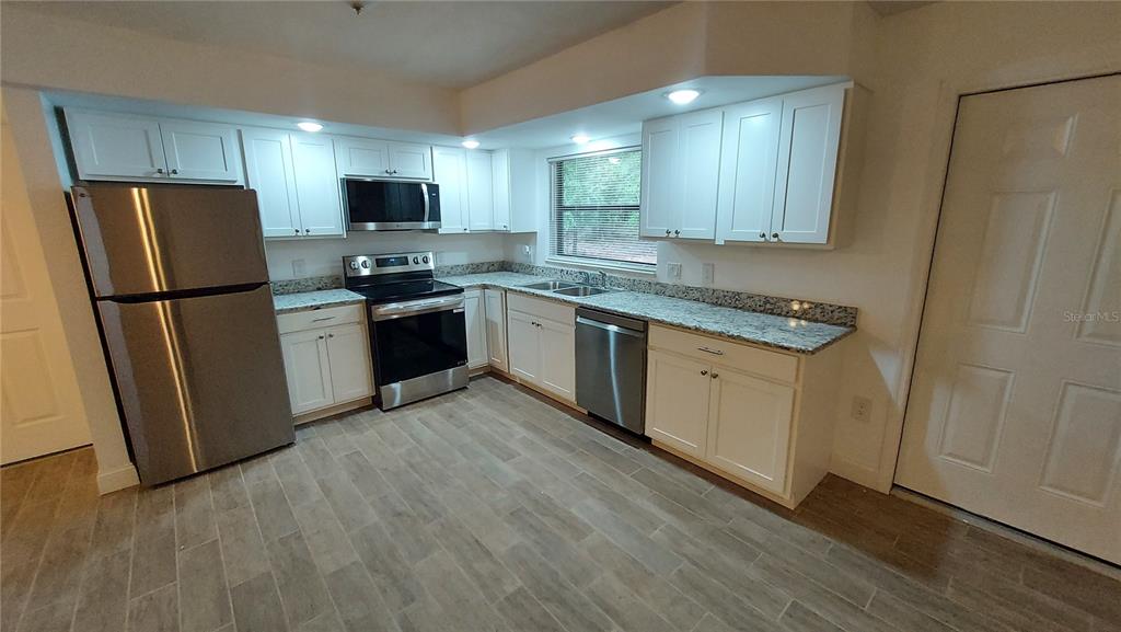 A kitchen features white cabinets, stainless steel appliances, granite countertops, and light-colored wood-look tile flooring — 9700 SW 209TH COURT, DUNNELLON, FL