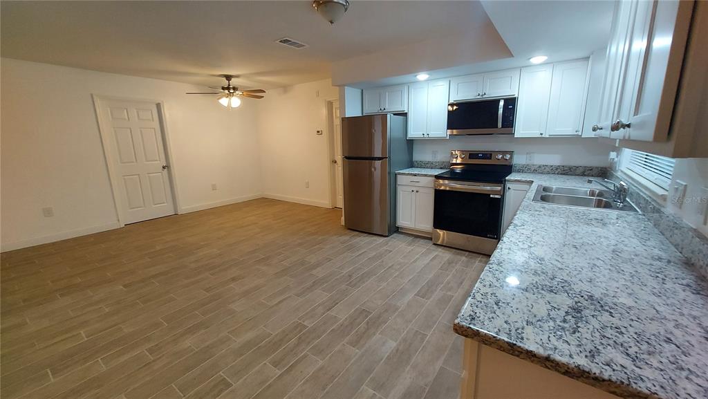 A kitchen with white cabinets, granite countertops, and stainless steel appliances opens to a dining area — 9700 SW 209TH COURT, DUNNELLON, FL